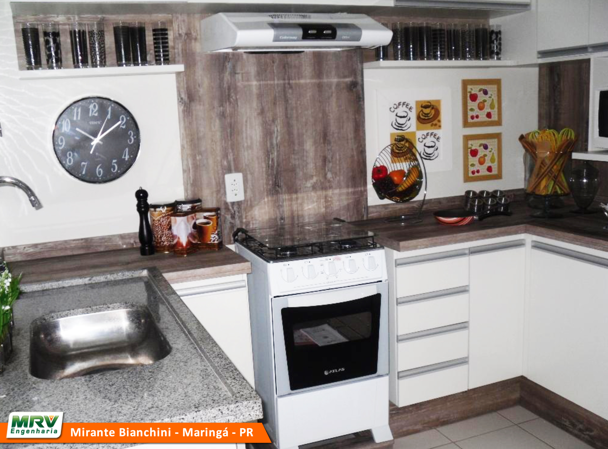 Cozinha montada com fogão, depurador de ar, armários brancos, pia de granito e com decorações e um relógio na parede