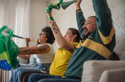 Quatro amigos vestidos de verde e amarelo agitando a bandeira do Brasil e comemorando o jogo da copa