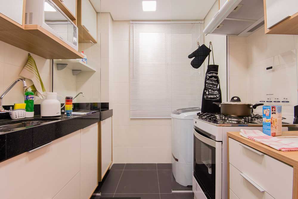 Vista lateral de uma cozinha conjugada com a lavanderia, sendo evidente eletrodomésticos, pia e janela de fundo.