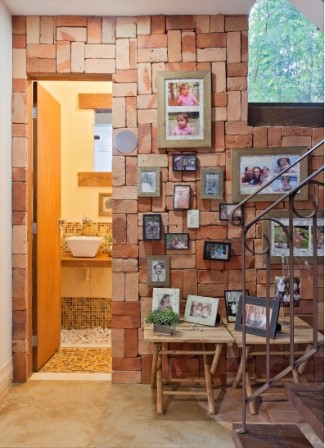 Parede de lavabo feita de tijolos a vista, com quadros de fotografias, duas mesinhas e uma escada logo a frente.