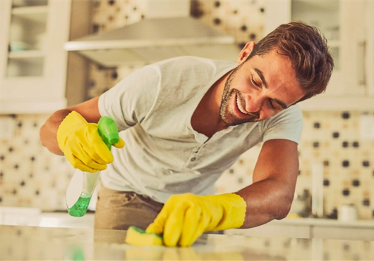 Homem limpando a bancada da cozinha de seu apartamento