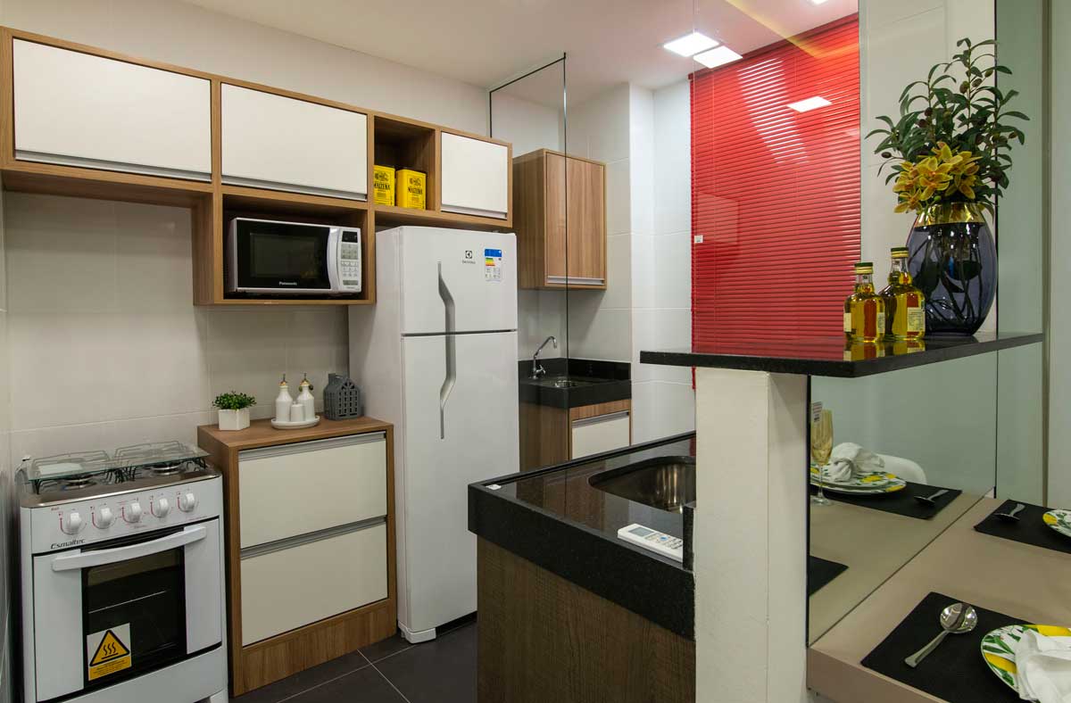 Cozinha com armários, fogão, balcão, geladeira e pia na parte aderida ao balcão em frente aos móveis.