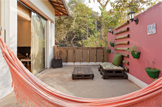 Área externa arborizada, com rede rosa, decorada com paletes, jardim vertical e quadro na parede.